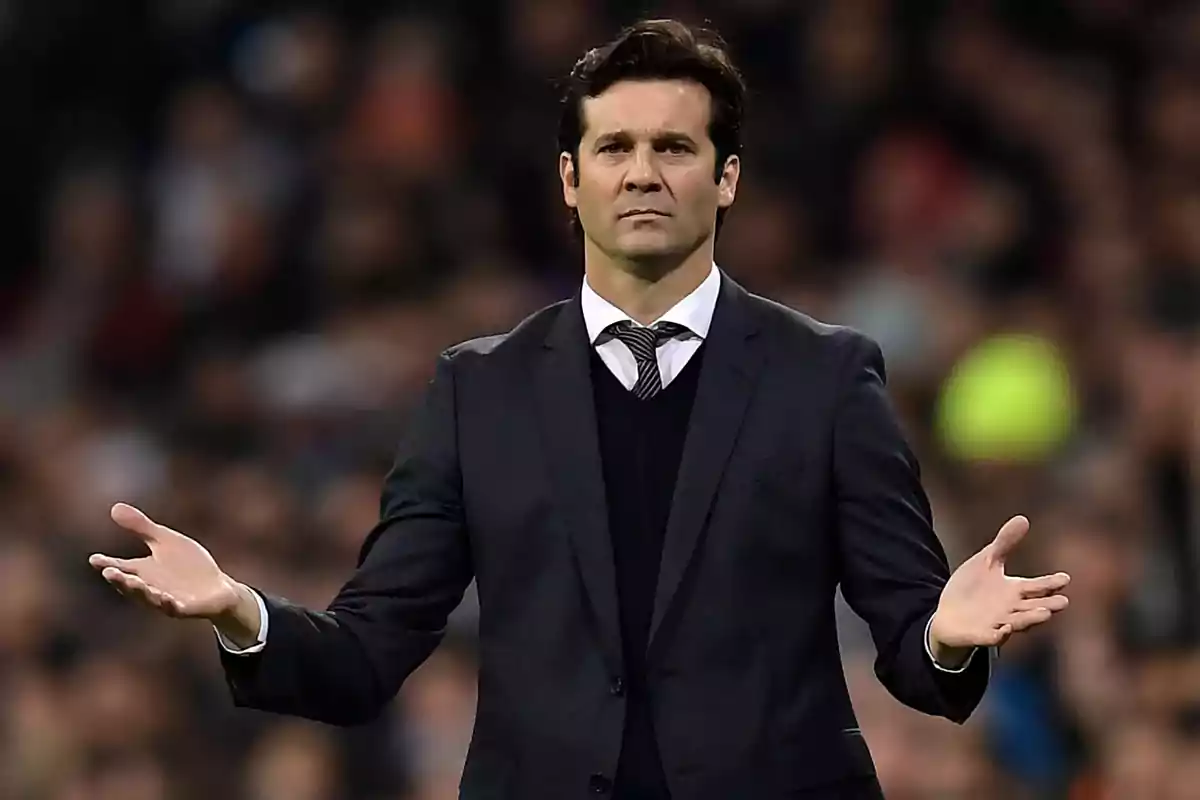 Man in a dark suit with a serious expression and arms outstretched in a stadium full of blurred people Man in a dark suit with a serious expression and arms outstretched in a stadium full of blurred people