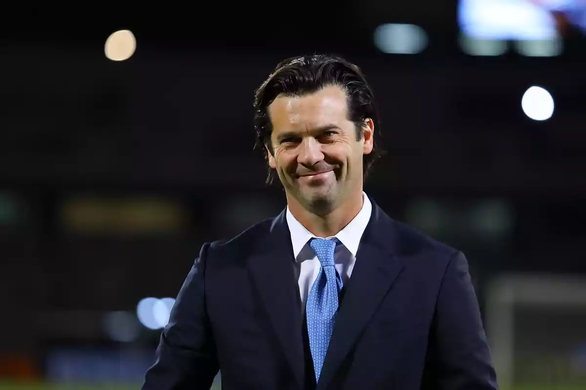 Dark-haired man in a suit and blue tie smiling in a nighttime setting Dark-haired man in a suit and blue tie smiling in a nighttime setting