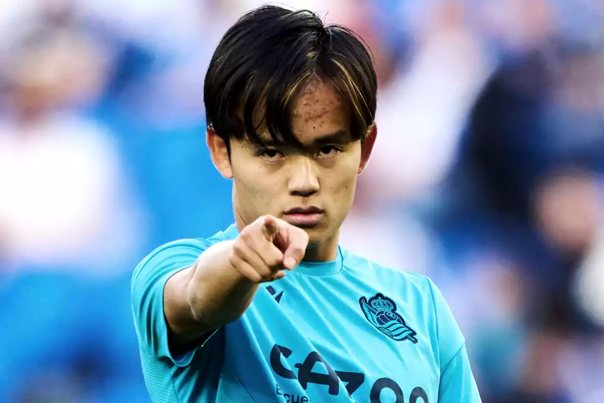 Un jugador de fútbol con camiseta azul señala hacia la cámara con una expresión seria. Un jugador de fútbol con camiseta azul señala hacia la cámara con una expresión seria.