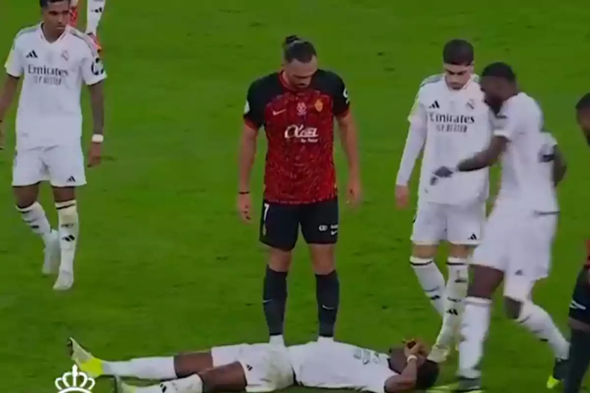 A soccer player lies on the ground while other players surround him on the field. A soccer player lies on the ground while other players surround him on the field.