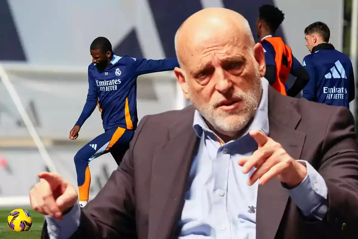 Un hombre calvo con barba gesticula mientras al fondo se observa a jugadores de fútbol entrenando con uniformes del Real Madrid.