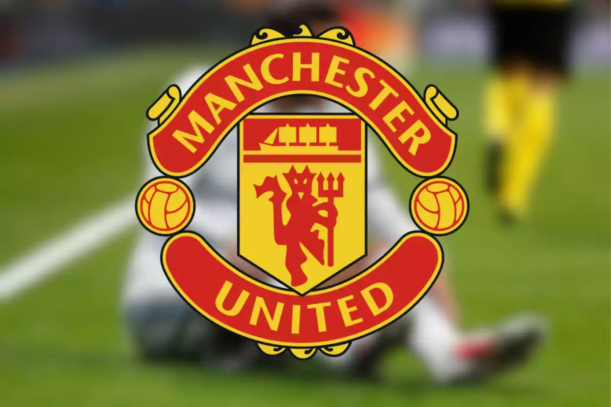 Escudo del Manchester United sobre un fondo desenfocado de un campo de fútbol.