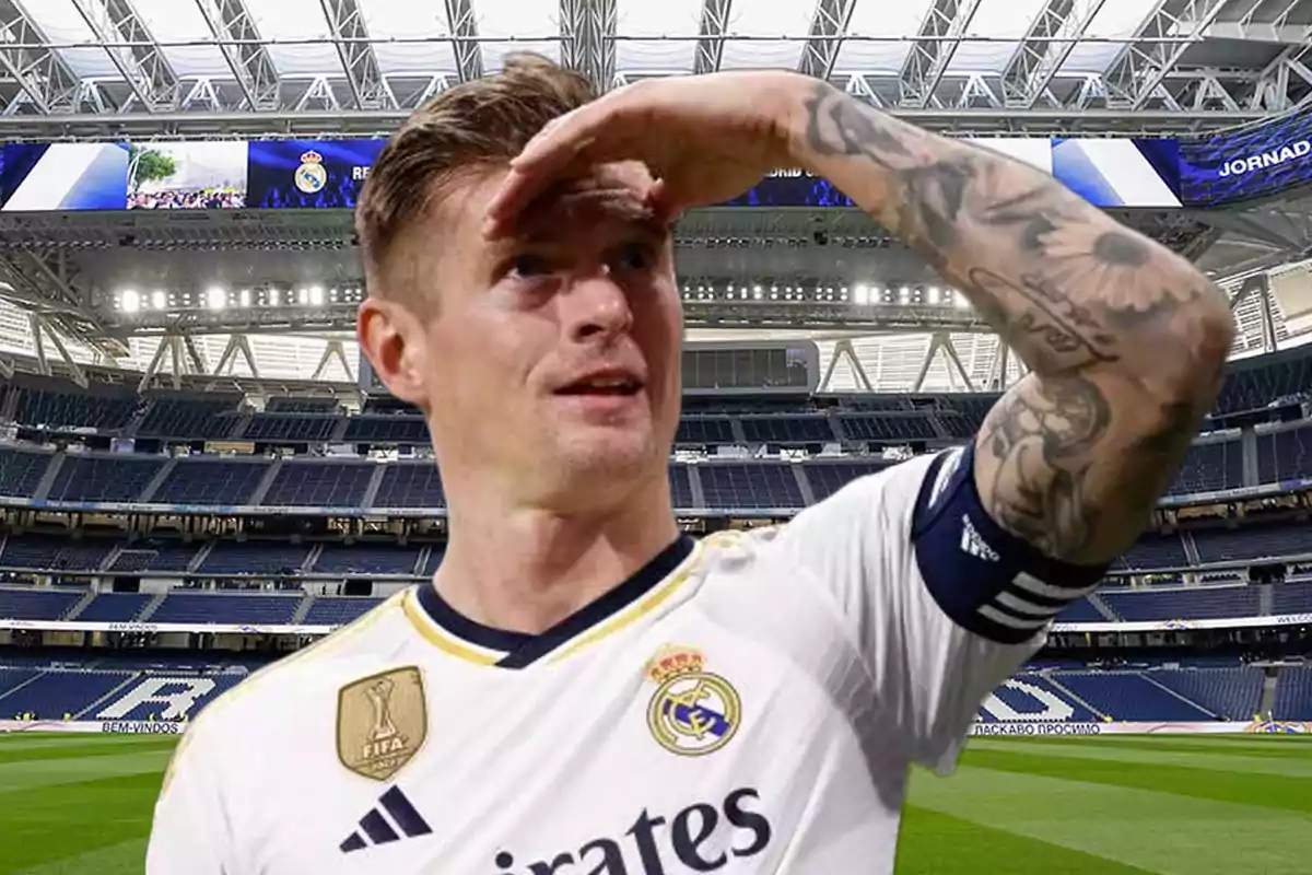 A player in a white uniform with tattoos on his right arm is in a stadium, looking toward the horizon with his hand on his forehead.