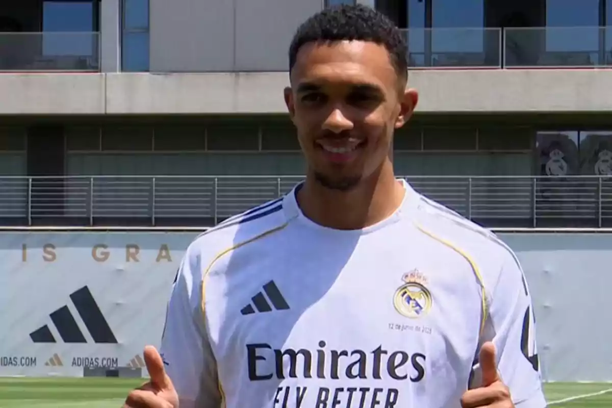 Soccer player wearing a white Real Madrid jersey smiles and gives two thumbs up on a training field