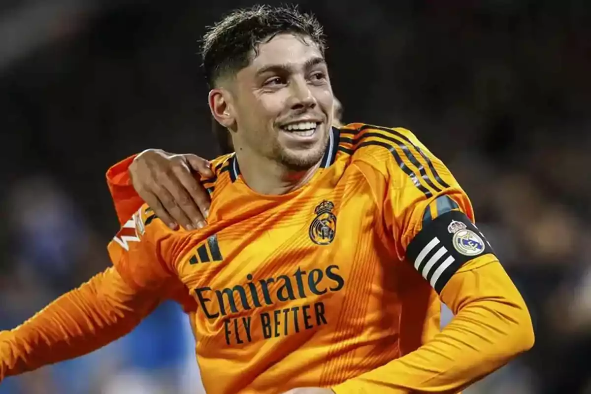 A soccer player in an orange Real Madrid uniform smiles as he is hugged by a teammate on the field. A soccer player in an orange Real Madrid uniform smiles as he is hugged by a teammate on the field.