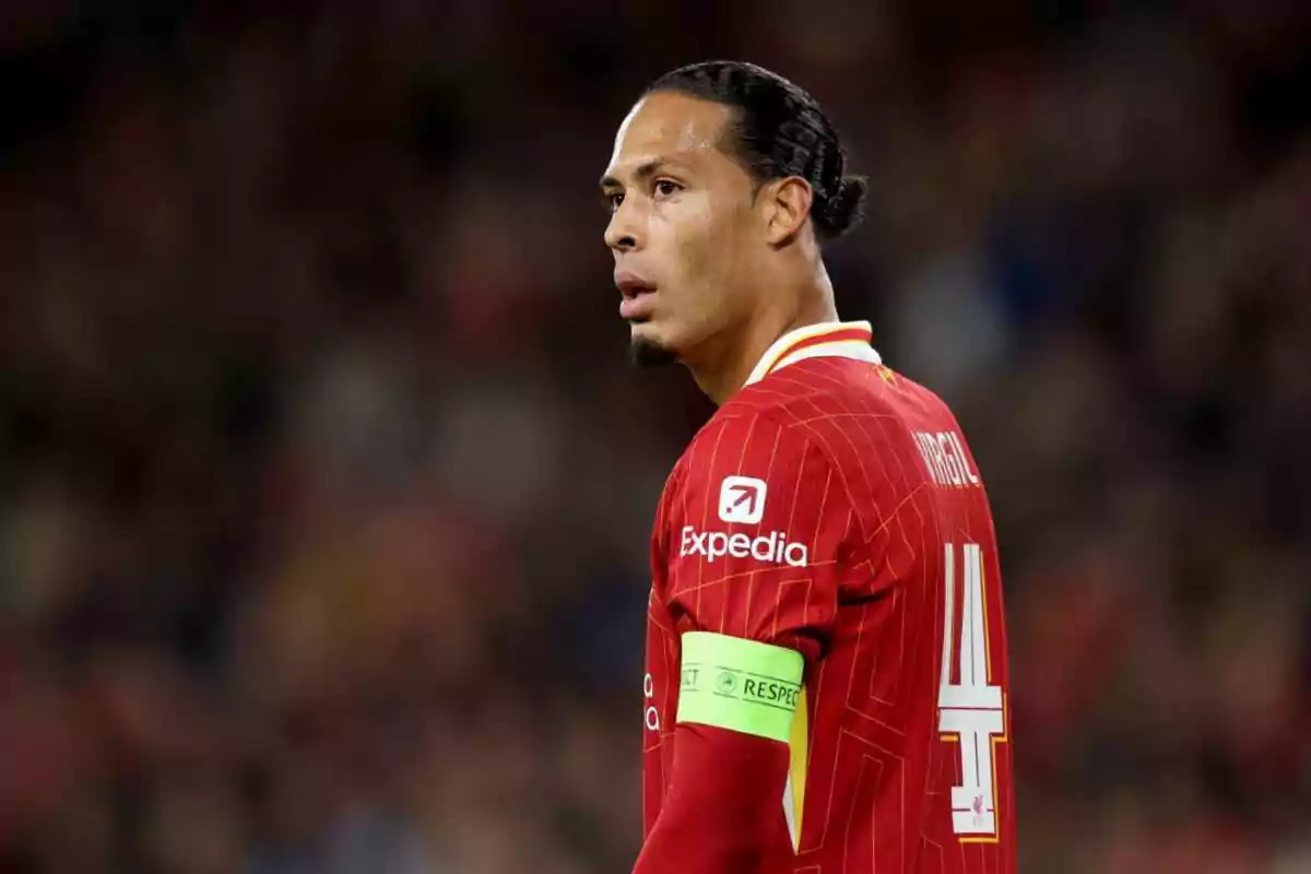 Jugador de fútbol con uniforme rojo y brazalete de capitán en un estadio.