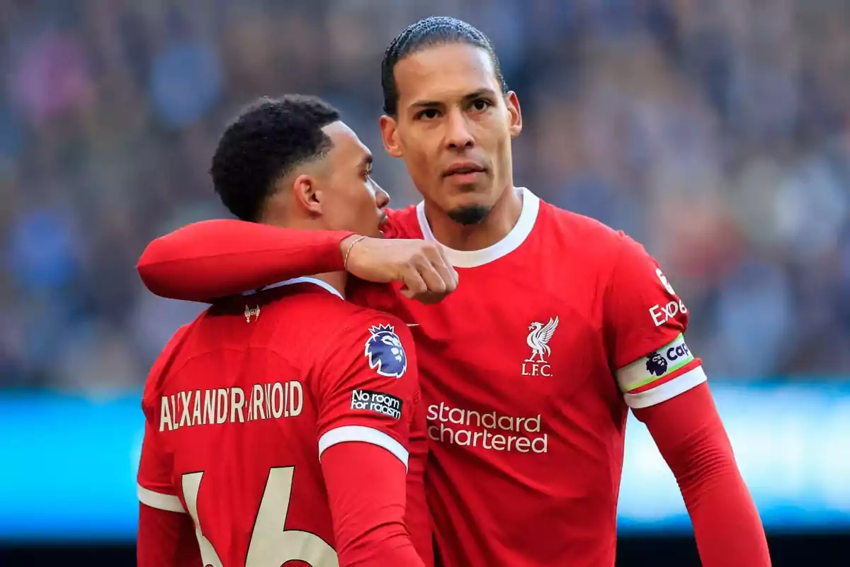 Dos jugadores del Liverpool con uniforme rojo en el campo de juego, uno de ellos con el brazo sobre el hombro del otro.