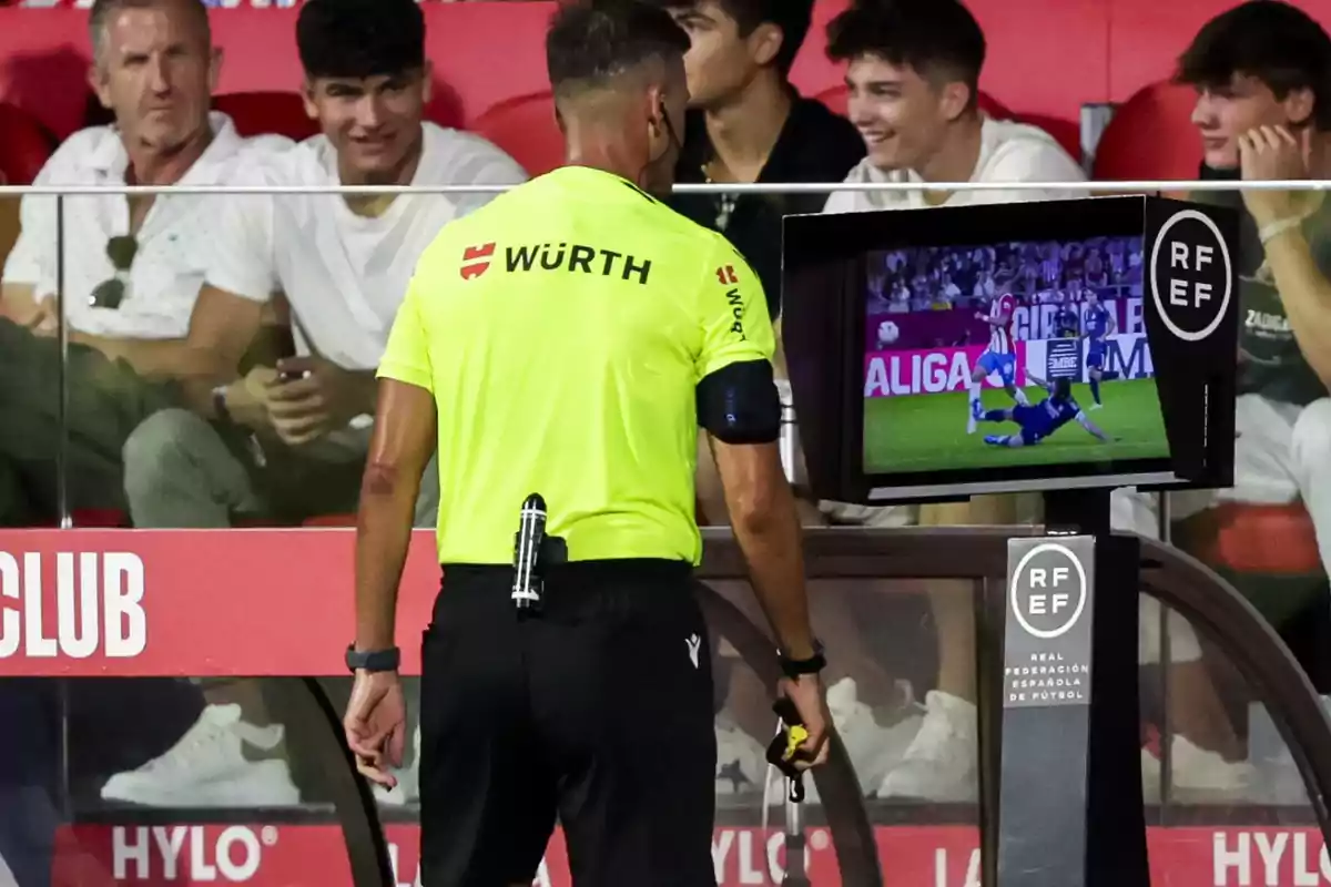 Un árbitro de fútbol revisa una jugada en el monitor del VAR mientras el público observa desde las gradas.