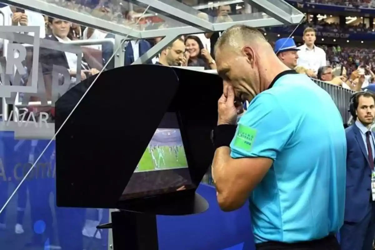 Soccer referee reviewing a play on the VAR monitor during a match with spectators watching in the background Soccer referee reviewing a play on the VAR monitor during a match with spectators watching in the background