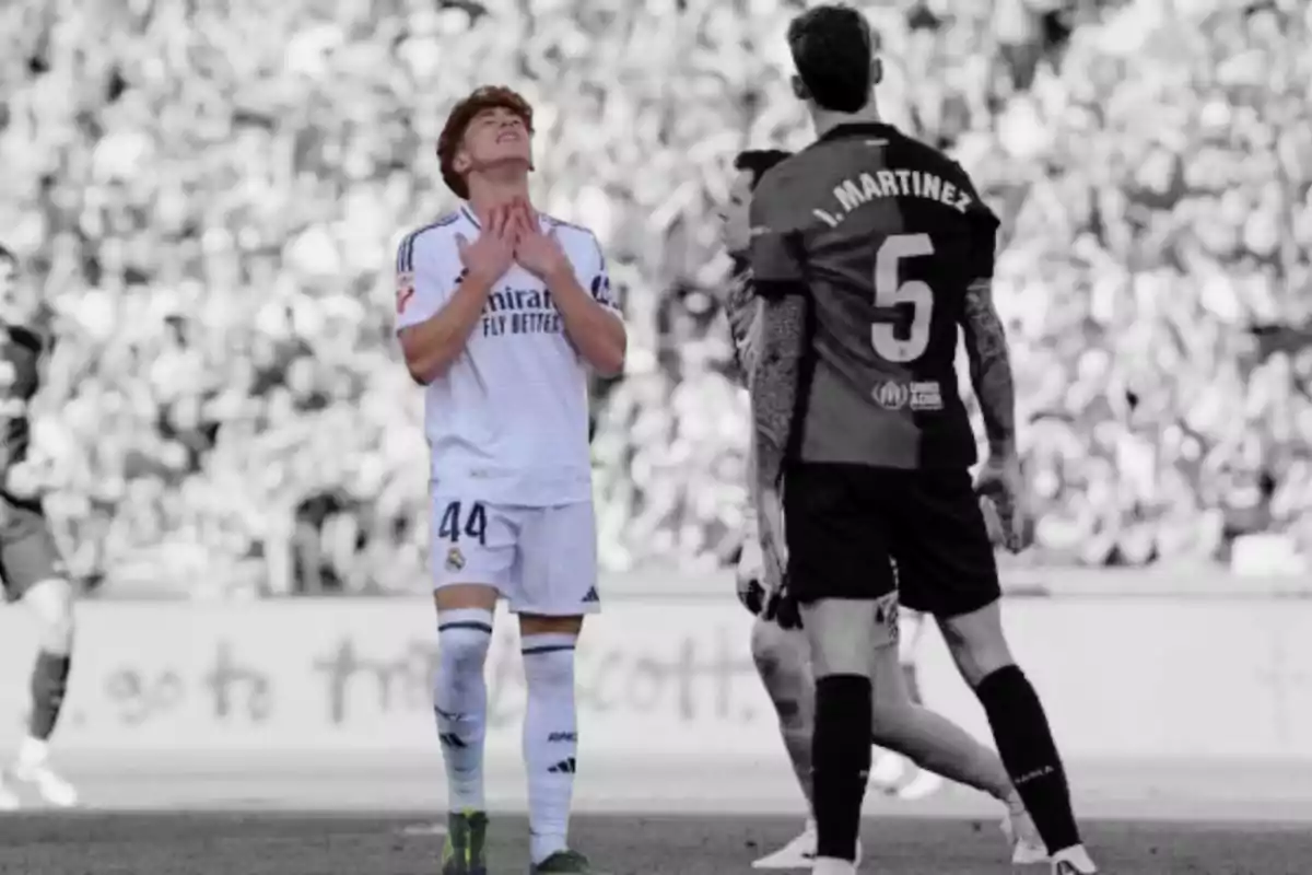 A player in a white uniform looks frustrated while another player in a dark uniform has his back turned on a soccer field.