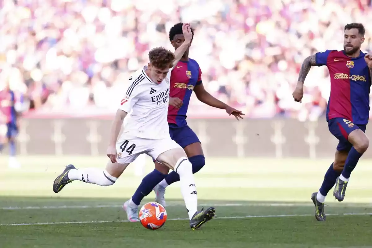 Un jugador del Real Madrid intenta patear el balón mientras dos jugadores del Barcelona intentan detenerlo durante un partido de fútbol. Un jugador del Real Madrid intenta patear el balón mientras dos jugadores del Barcelona intentan detenerlo durante un partido de fútbol.