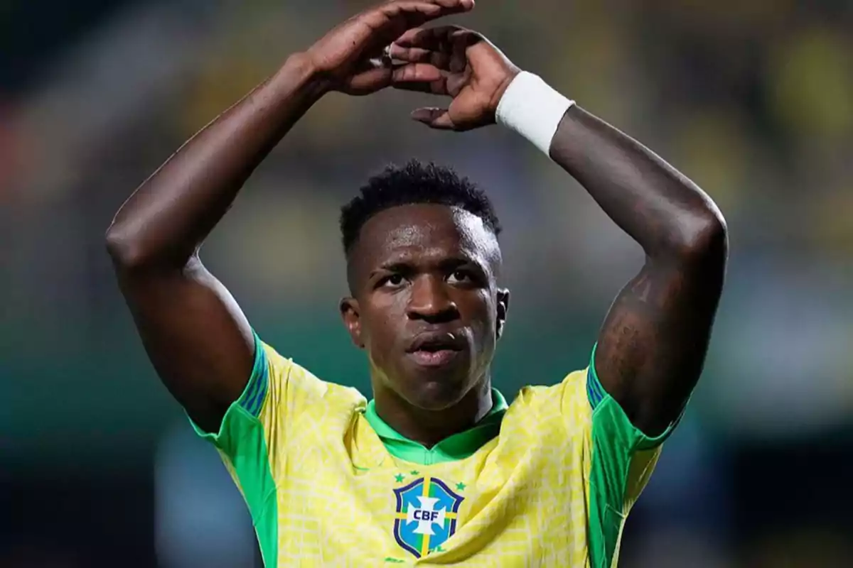 Jugador de fútbol con uniforme amarillo y verde levantando los brazos en un gesto durante un partido.