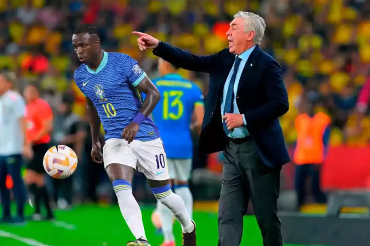 A player wearing the Brazil uniform chases the ball while a coach in a suit gives him instructions on the field during a match.