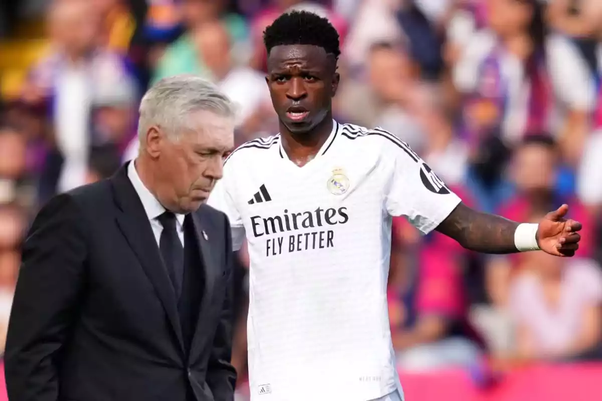 A soccer coach in a dark suit walks with his head down while a player in a white Real Madrid uniform gestures on the field.