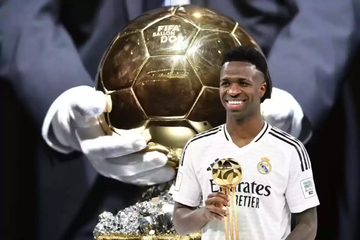 Un jugador de fútbol sonriente con el uniforme del Real Madrid sostiene un trofeo dorado frente a un gran Balón de Oro sostenido por manos enguantadas.