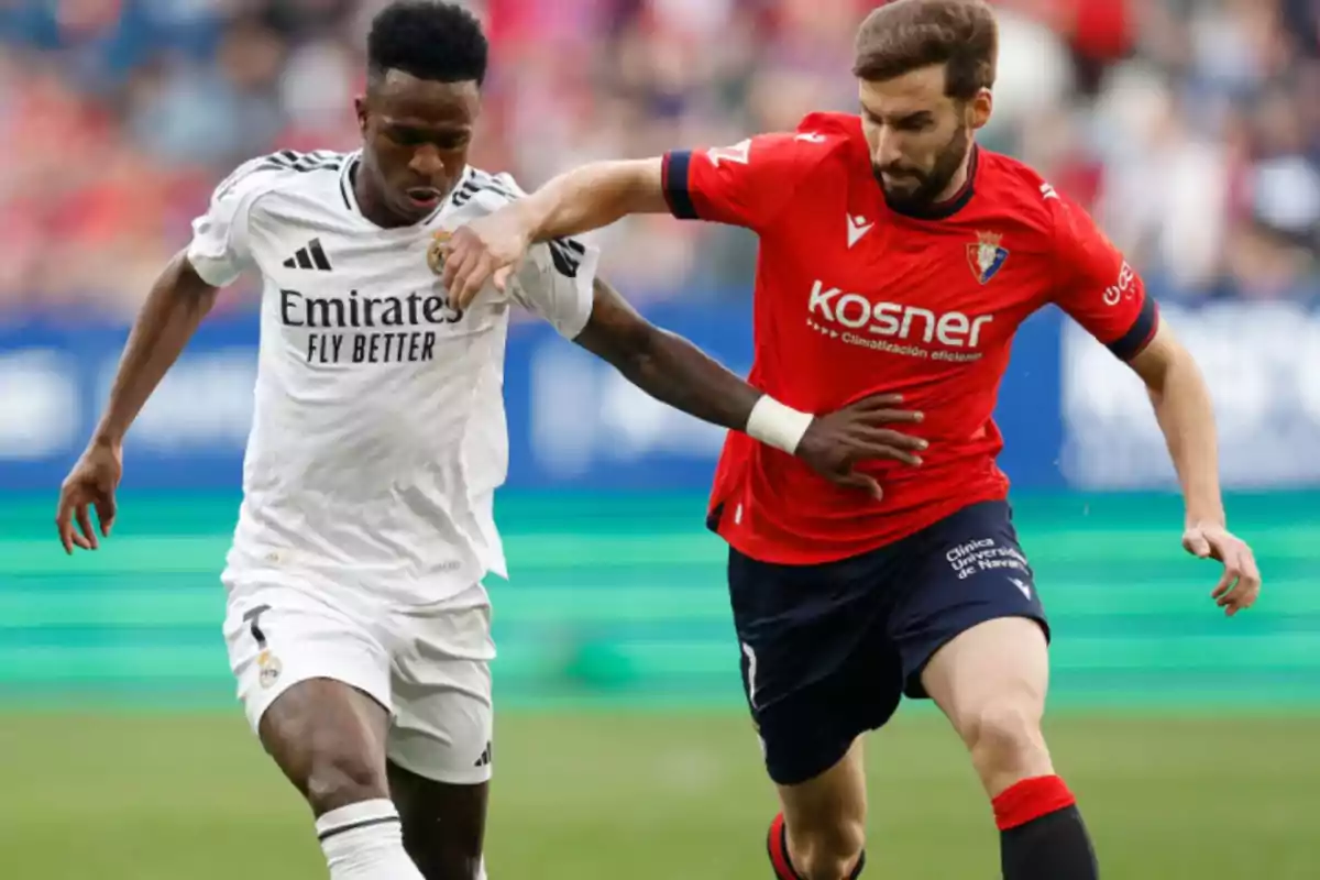 Two players compete for the ball in a match, one wearing white and the other red.