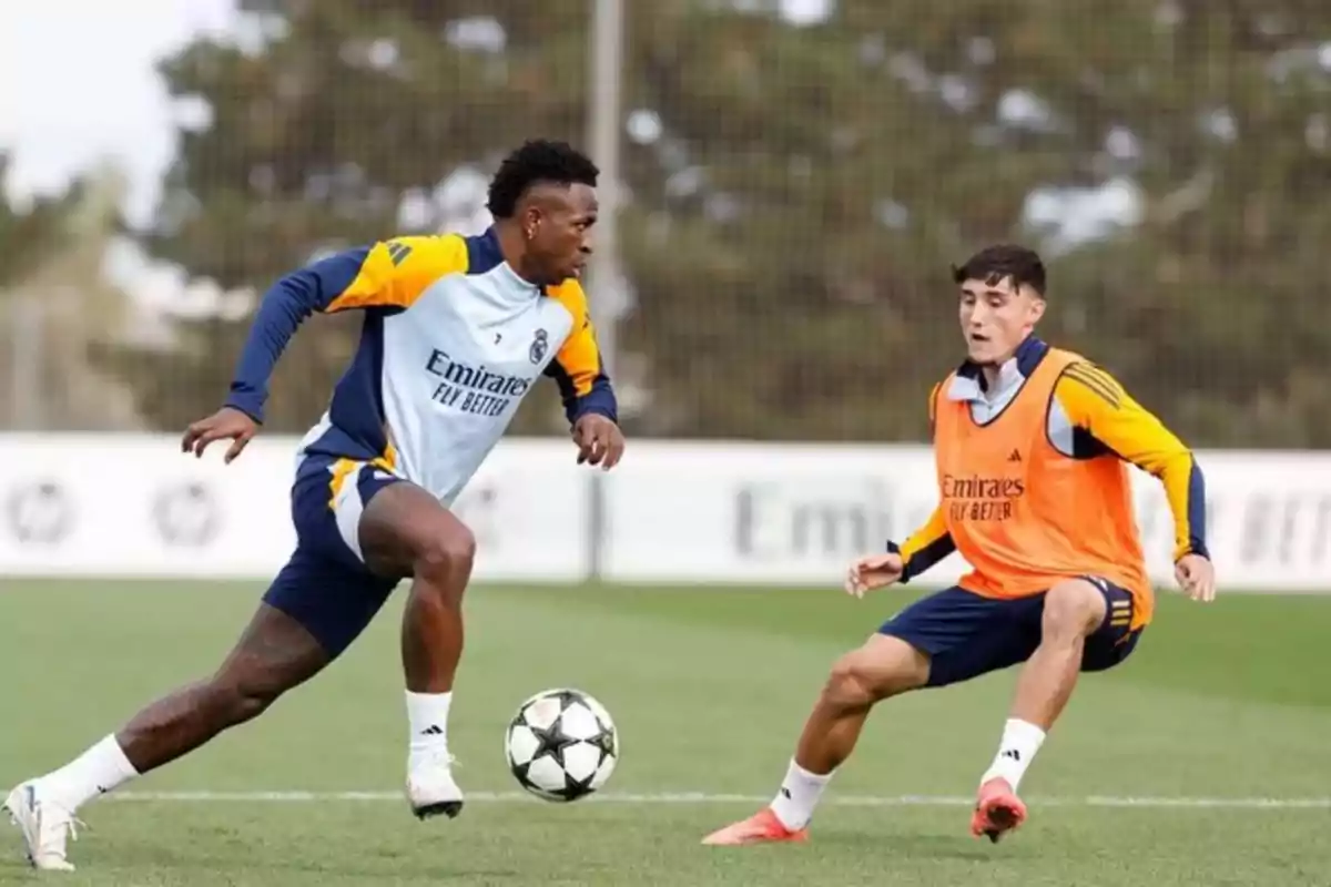 Two soccer players training on a field, one in an orange bib and the other in a blue and yellow training uniform, while fighting for the ball.