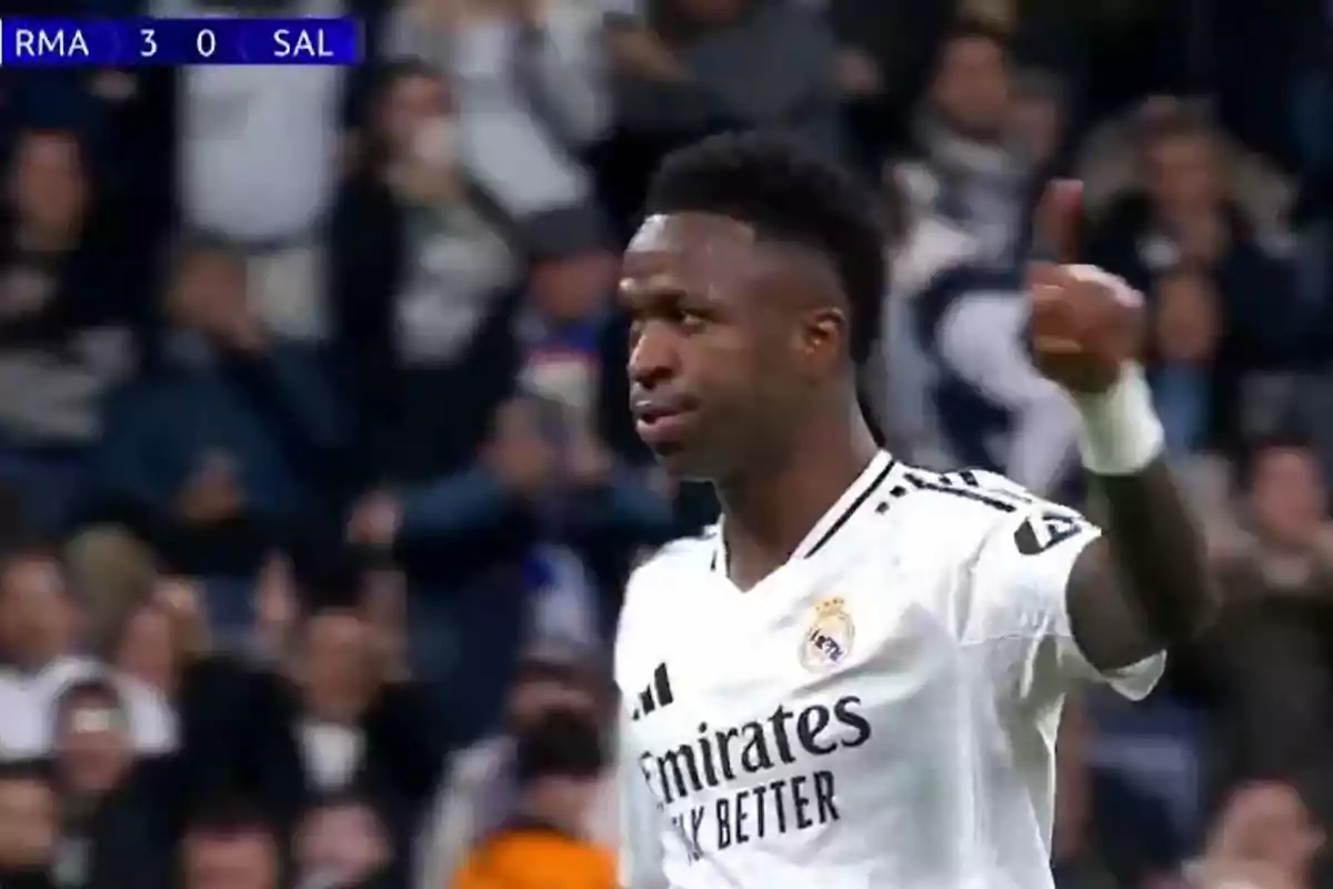 A football player wearing a white Real Madrid jersey gives a thumbs up during a match, with the scoreboard showing 3-0 in favor of his team.