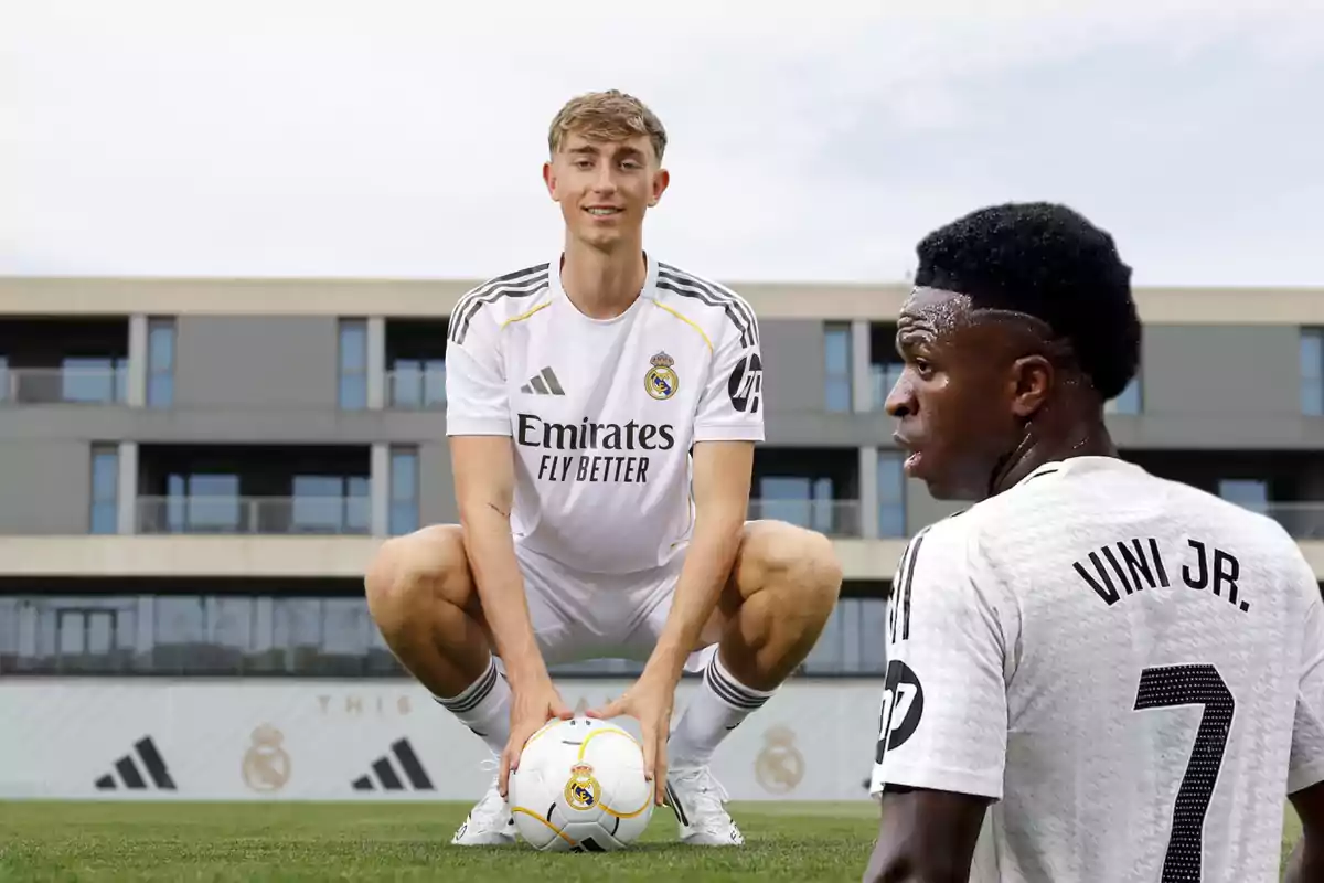 Two Real Madrid players on the training field, one crouching and holding a ball and the other with his back turned, wearing a jersey that shows the name Vini Jr.