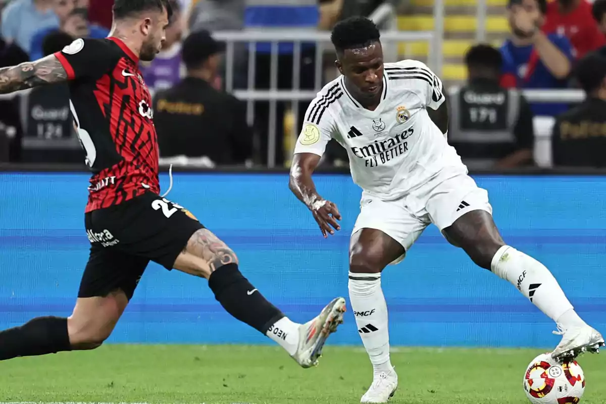 Two soccer players compete for the ball in a game, one in a white uniform and the other in a red and black uniform. Two soccer players compete for the ball in a game, one in a white uniform and the other in a red and black uniform.