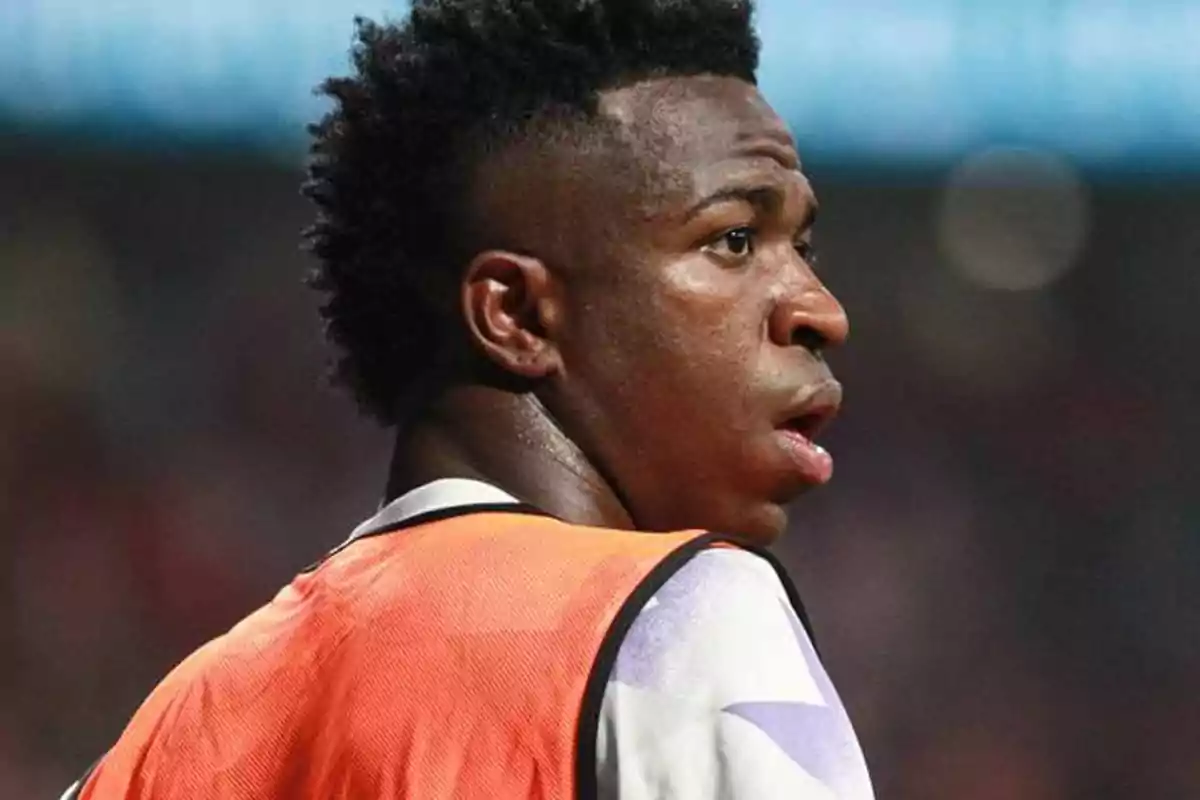 A soccer player in an orange vest looks to the side during a match.