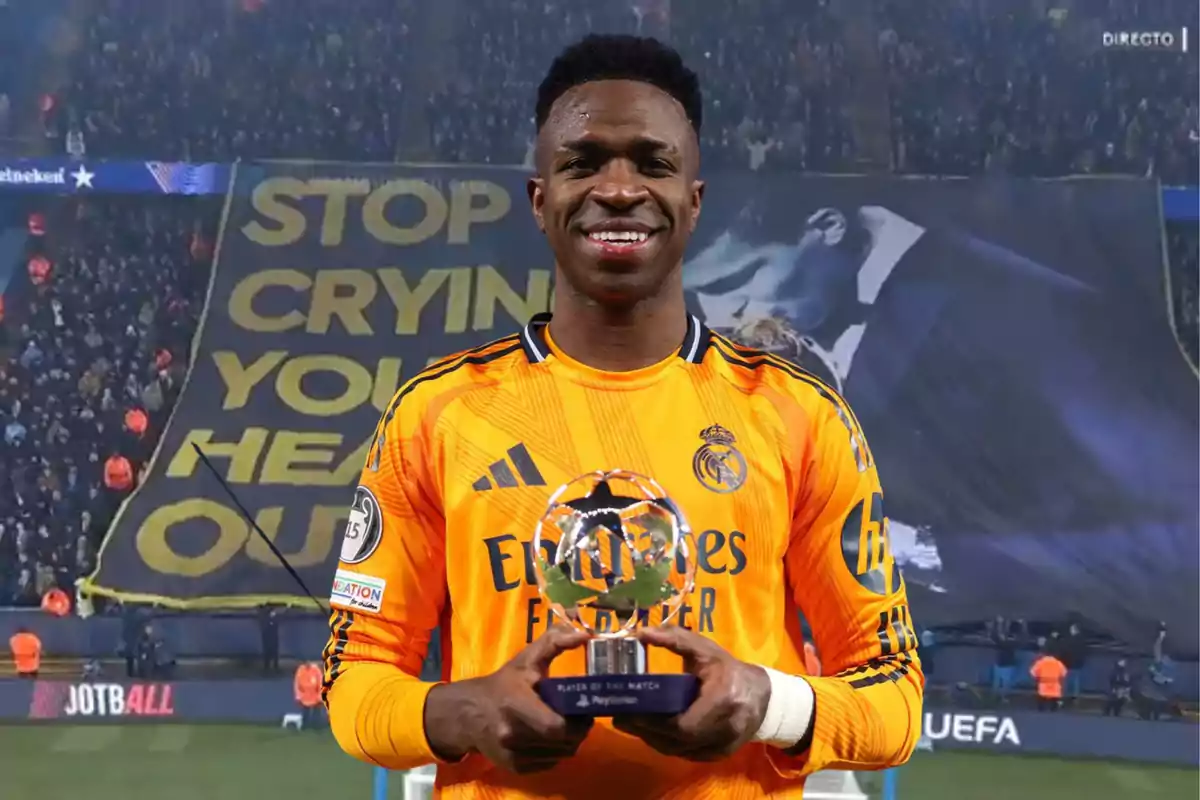 A player in an orange uniform holds a trophy in front of a banner in a stadium full of spectators.