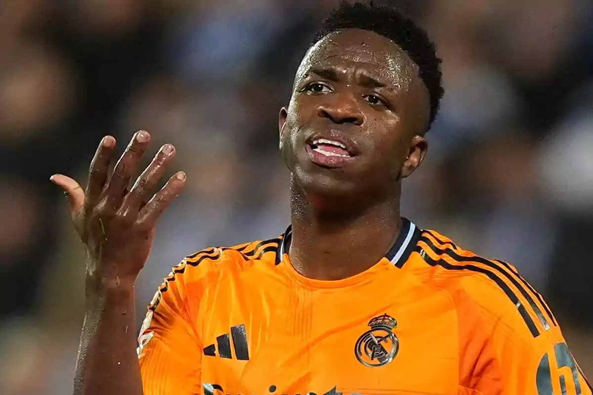 Football player in orange Real Madrid uniform gesturing on the field.