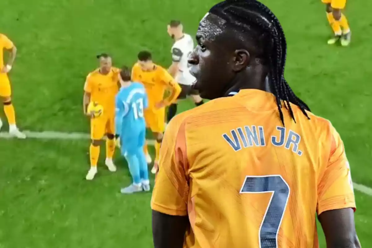 A soccer player with the name "VINI JR." on his jersey looks out at a scene on the field where other players are gathered.