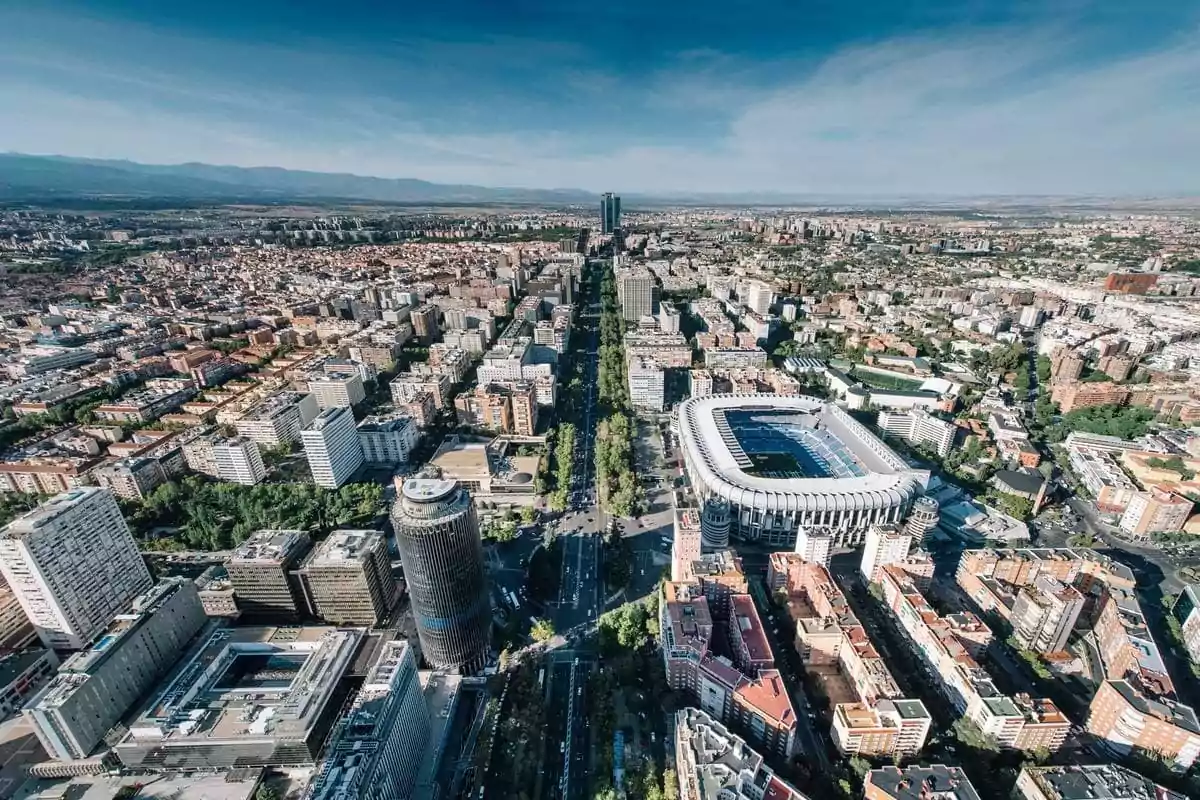 Vista aérea de una ciudad con un estadio grande y edificios altos rodeados de calles y vegetación. Vista aérea de una ciudad con un estadio grande y edificios altos rodeados de calles y vegetación.