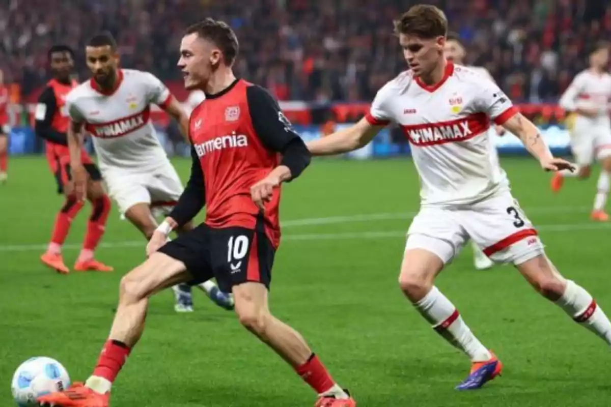 Two soccer players compete for the ball in a game, one wearing a red and black uniform and the other wearing a white and red uniform. Two soccer players compete for the ball in a game, one wearing a red and black uniform and the other wearing a white and red uniform.