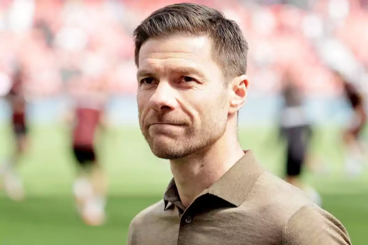 A man with a short beard and light brown hair is standing outdoors with a blurred background of people and grass. A man with a short beard and light brown hair is standing outdoors with a blurred background of people and grass.