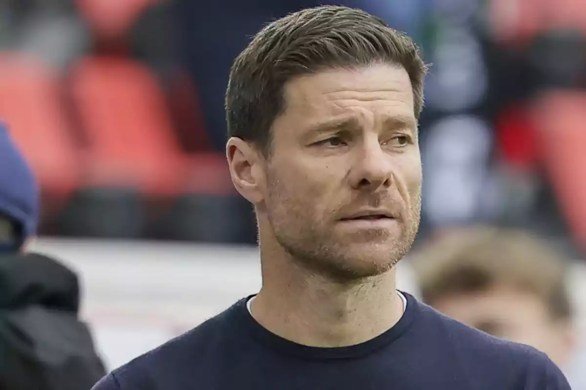 Hombre de cabello corto y barba ligera con expresión seria en un entorno deportivo Hombre de cabello corto y barba ligera con expresión seria en un entorno deportivo