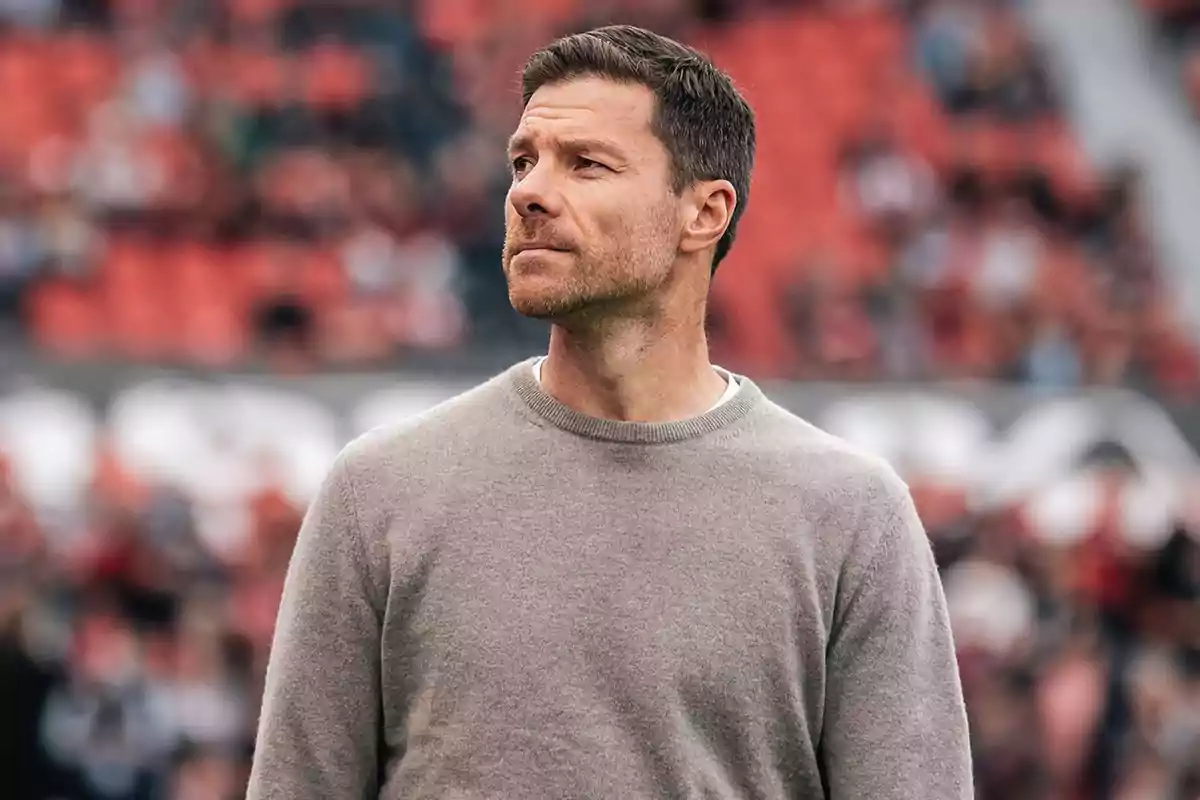 A man in a grey sweater looks pensively to the side in a stadium with out-of-focus red seats in the background. A man in a grey sweater looks pensively to the side in a stadium with out-of-focus red seats in the background.