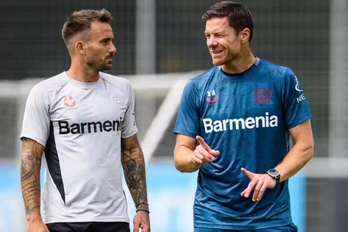 Dos hombres con ropa deportiva del Bayer Leverkusen conversan en un campo de entrenamiento Dos hombres con ropa deportiva del Bayer Leverkusen conversan en un campo de entrenamiento