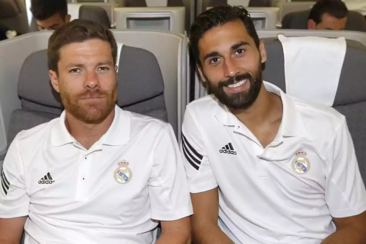 Two men in white Real Madrid jerseys sitting on a plane.