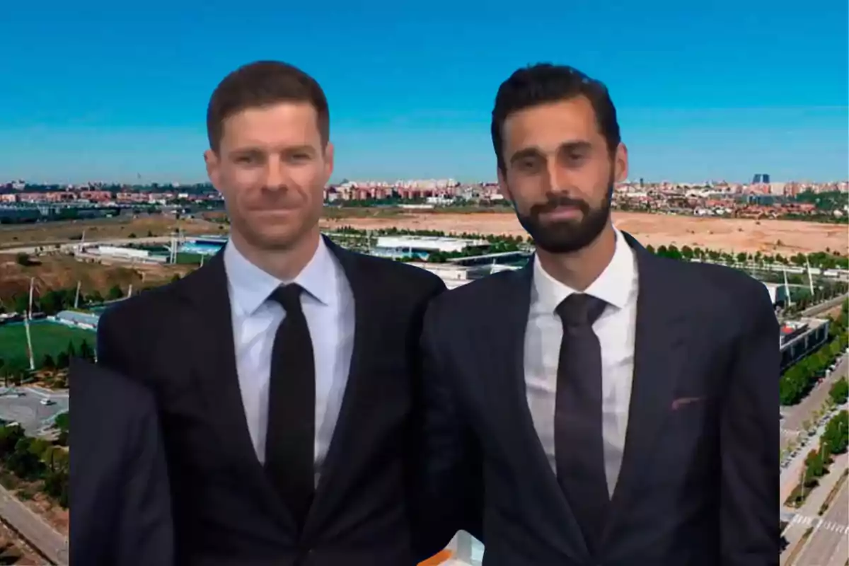 Two men dressed in suits and ties pose together in front of an urban landscape with a clear sky.