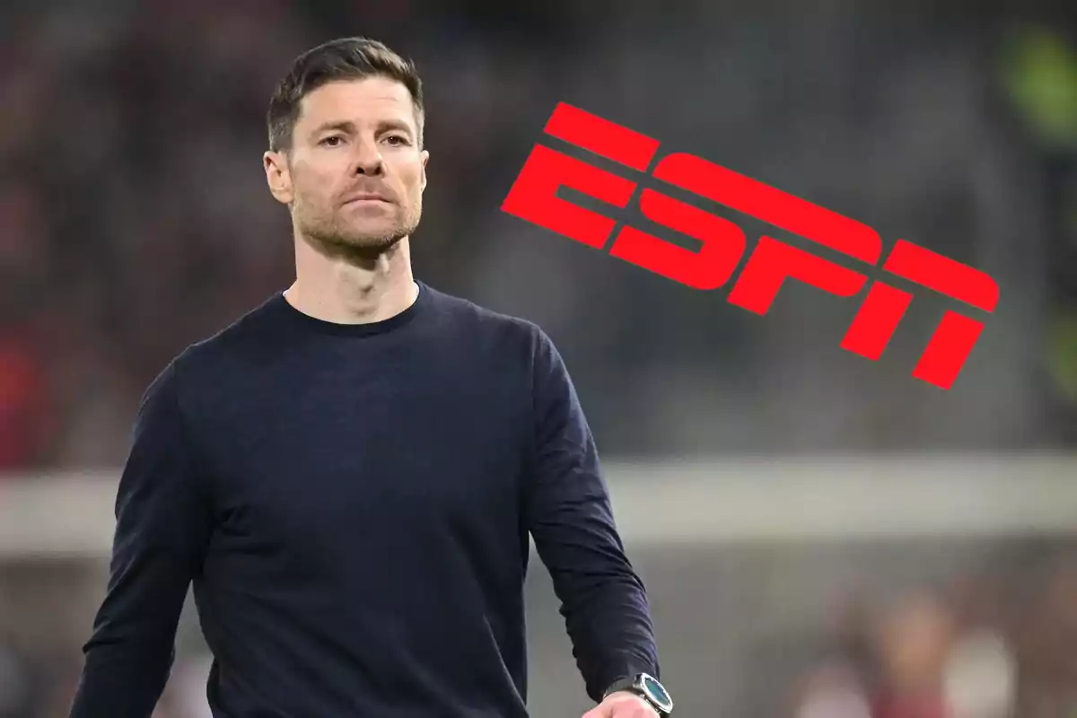 A man in a dark sweater and a watch on his wrist walks in front of a blurred background with the ESPN logo in red.