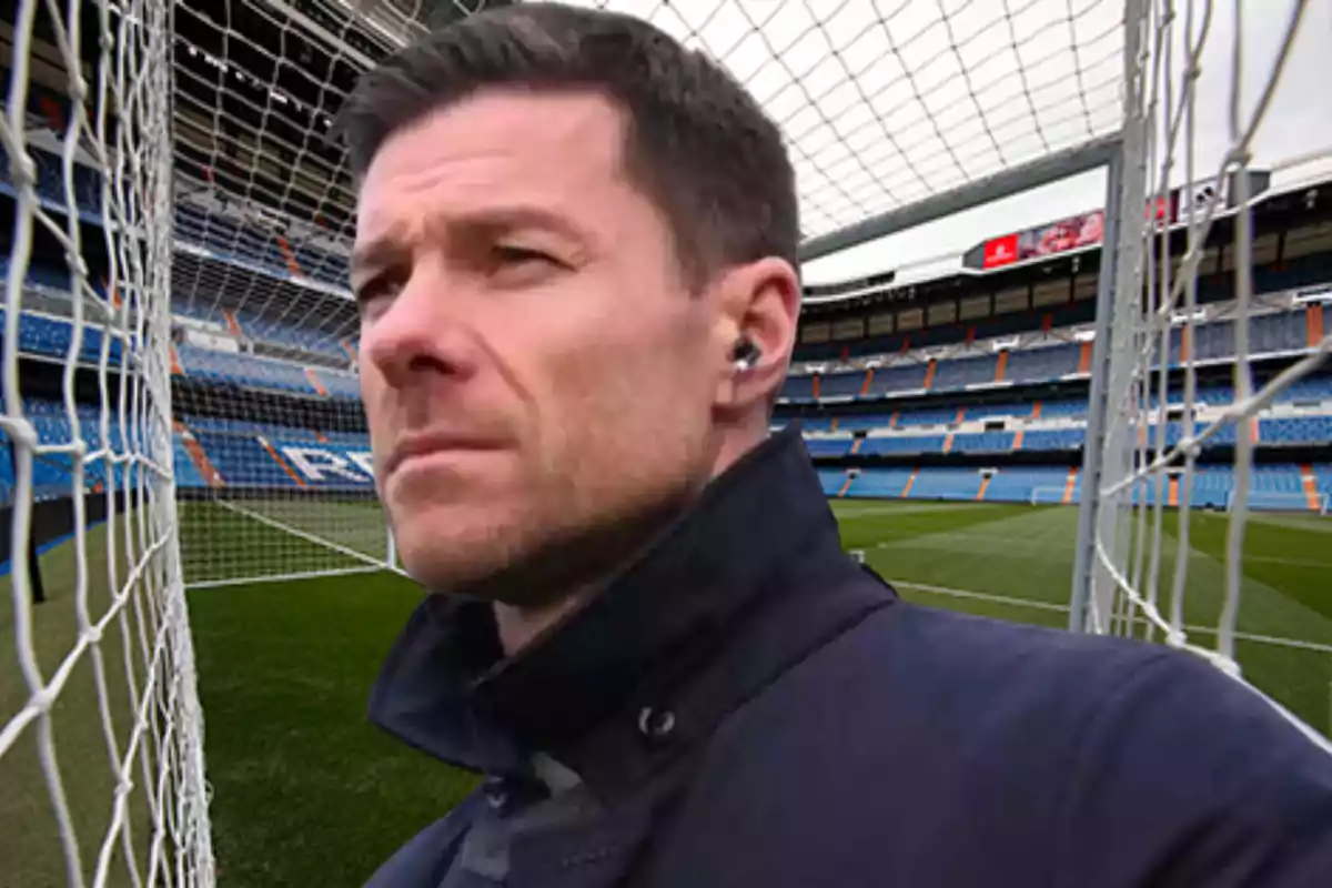 Un hombre con auriculares de pie junto a una portería en un estadio de fútbol vacío.