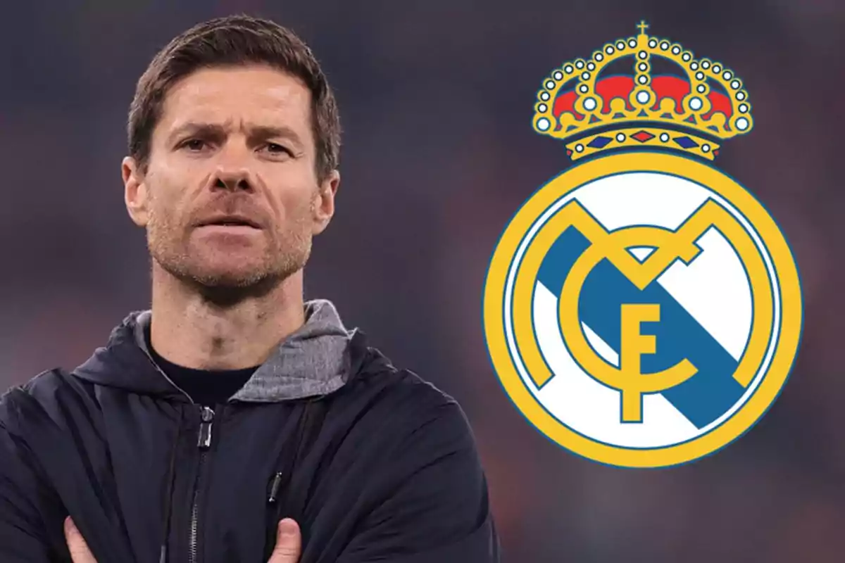 Un hombre con chaqueta oscura está de pie junto al escudo del Real Madrid.