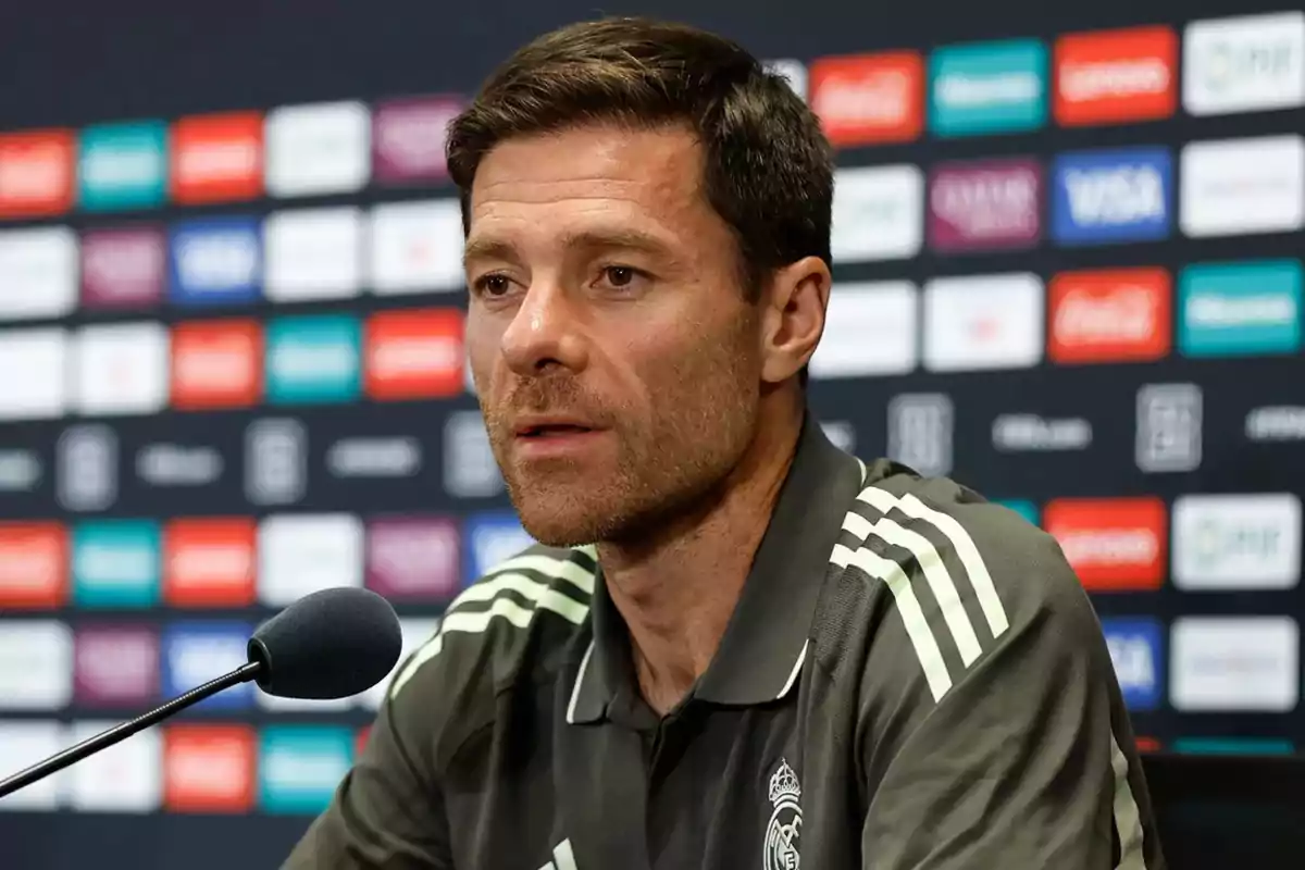 Hombre con camiseta deportiva de color oscuro hablando en una conferencia de prensa con fondo de logotipos de patrocinadores. Hombre con camiseta deportiva de color oscuro hablando en una conferencia de prensa con fondo de logotipos de patrocinadores.