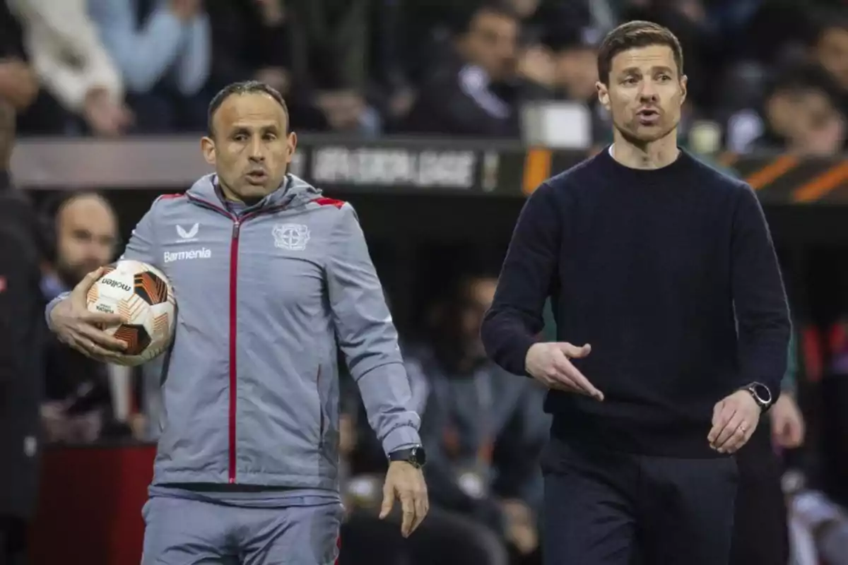 Dos hombres en un campo de fútbol, uno con un balón en la mano y el otro gesticulando. Dos hombres en un campo de fútbol, uno con un balón en la mano y el otro gesticulando.
