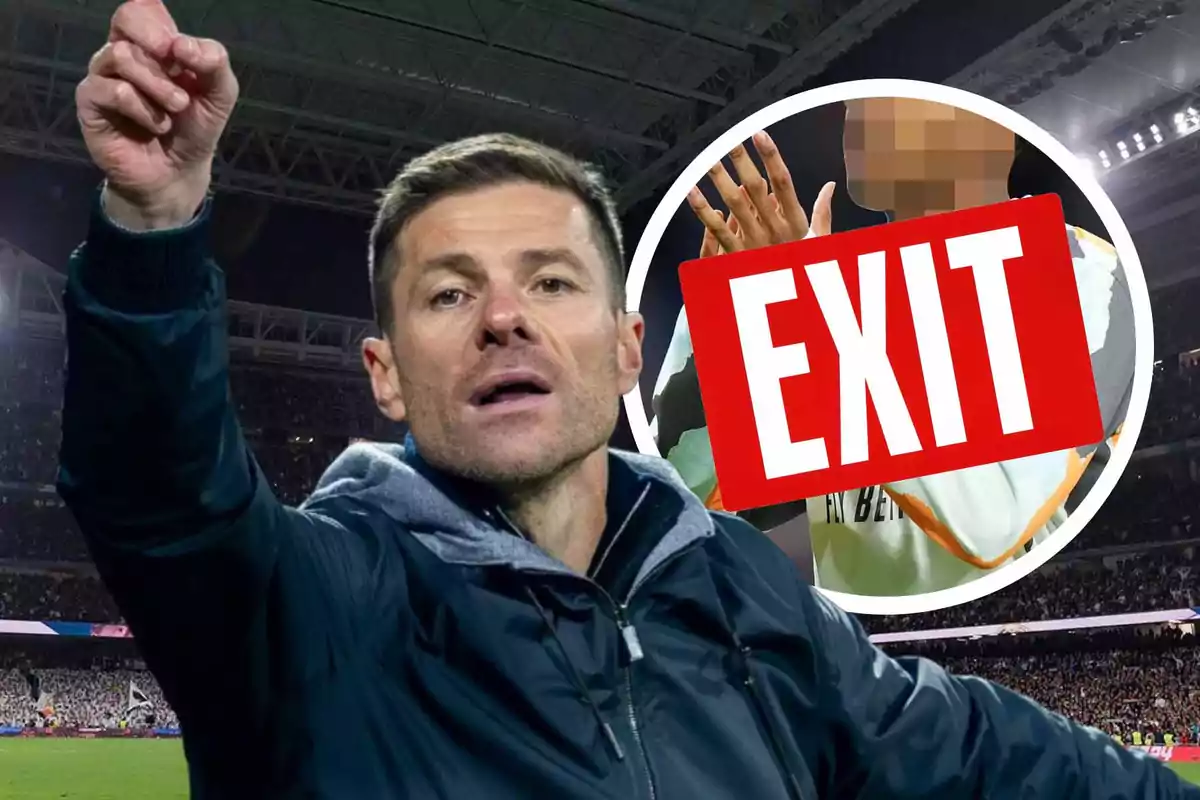 A man in a dark jacket gestures in a soccer stadium while a red sign with the word "EXIT" partially covers another person in the background.
