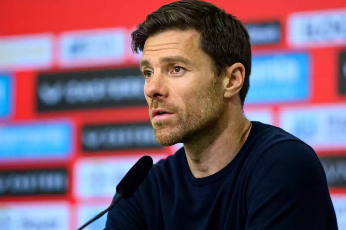 A man speaking at a press conference with a red and black background.