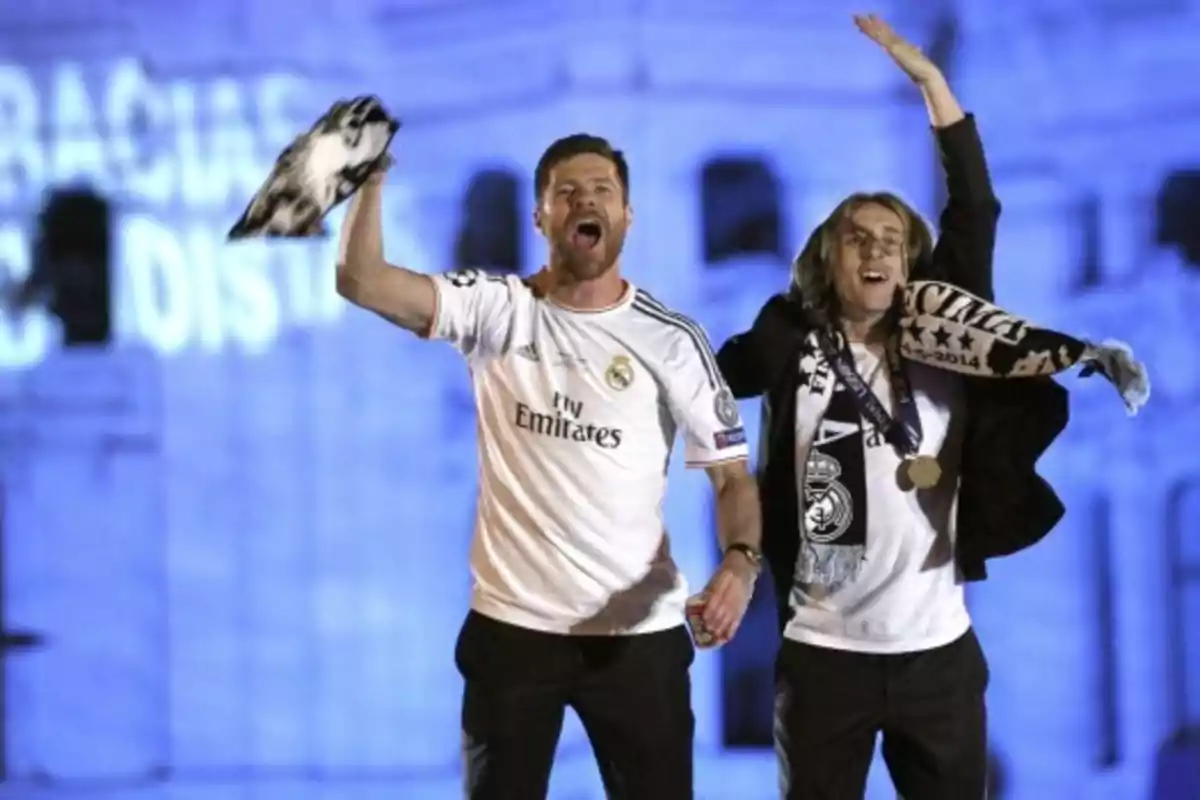 Two people celebrate with Real Madrid scarves and jerseys at a nighttime event. Two people celebrate with Real Madrid scarves and jerseys at a nighttime event.