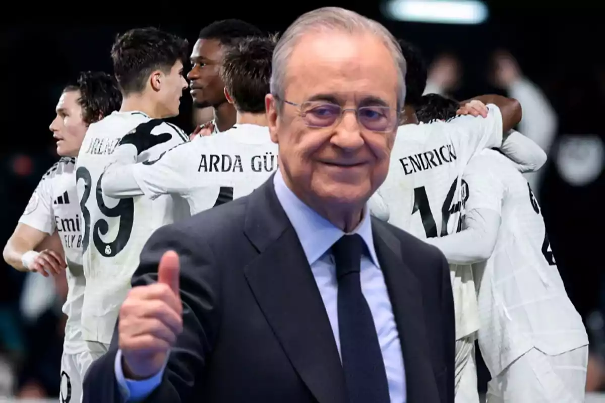 Un hombre mayor con gafas y traje sonríe y levanta el pulgar mientras un grupo de jugadores de fútbol se abraza en el fondo.