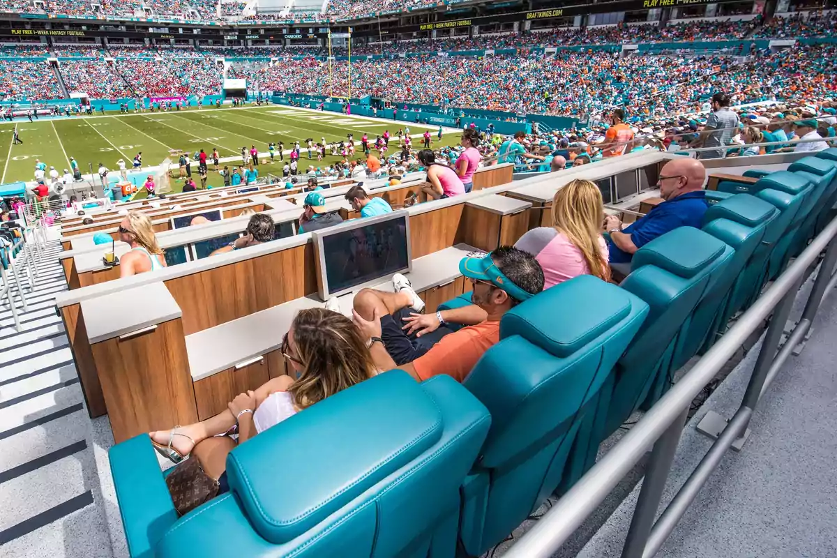 People sitting in comfortable top-level seats with individual screens while enjoying an American football game in a stadium full of spectators