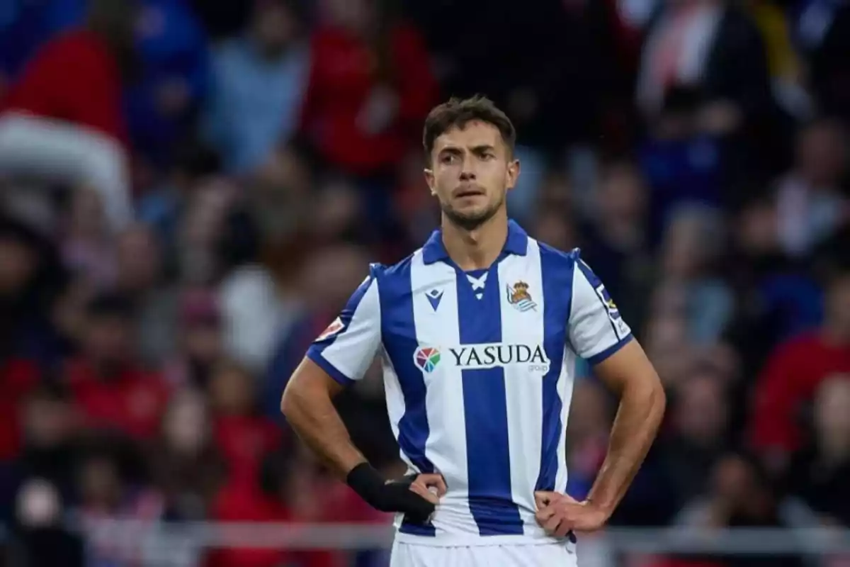 Soccer player wearing a Real Sociedad uniform on the field during a match with hands on hips and a serious expression Soccer player wearing a Real Sociedad uniform on the field during a match with hands on hips and a serious expression
