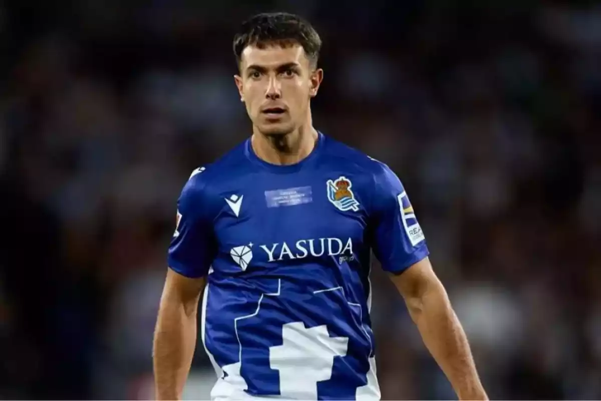 Jugador de fútbol con camiseta azul de la Real Sociedad en el campo de juego. Jugador de fútbol con camiseta azul de la Real Sociedad en el campo de juego.