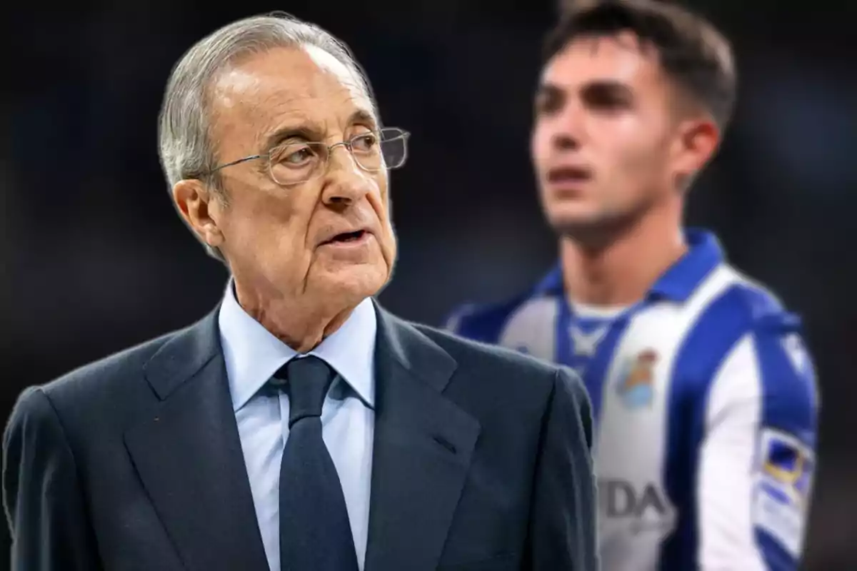 An older man with glasses and a dark suit in the foreground, with a soccer player out of focus in the background.